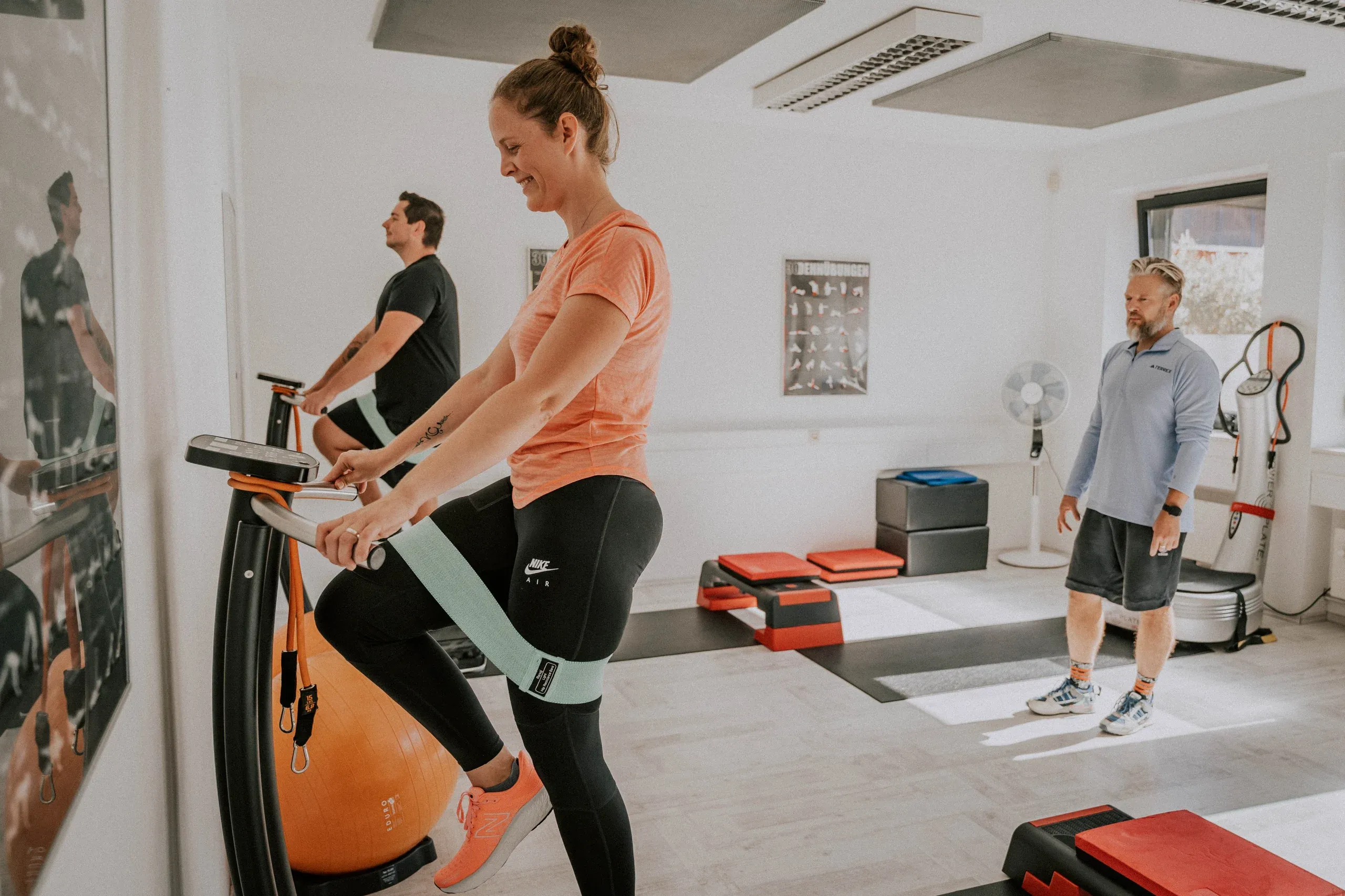 Eine Frau trainiert lächelnd auf dem Rad, ein Fitnessband um die Oberschenkel